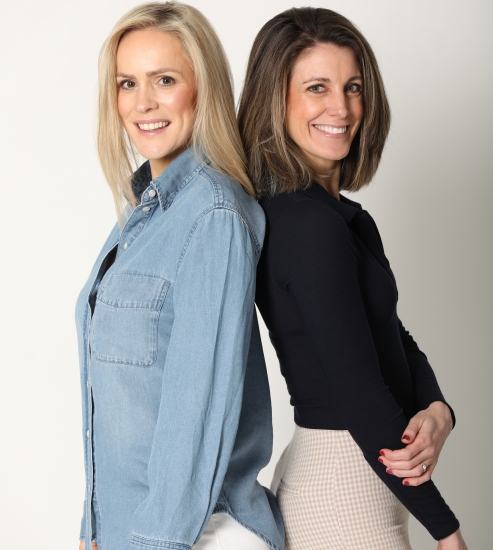 Two yoga teachers standing back to back and smiling, representing the YogaCourse team